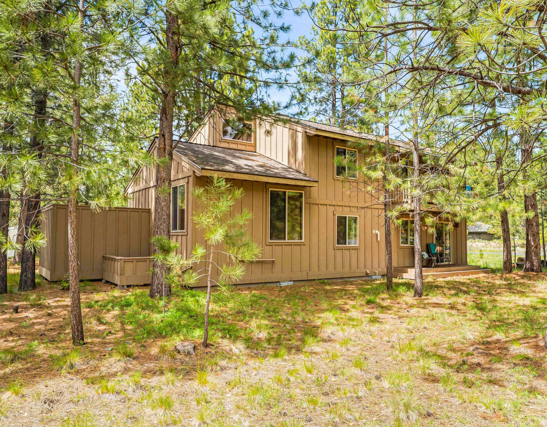 Exterior view of a tan house among pine trees.