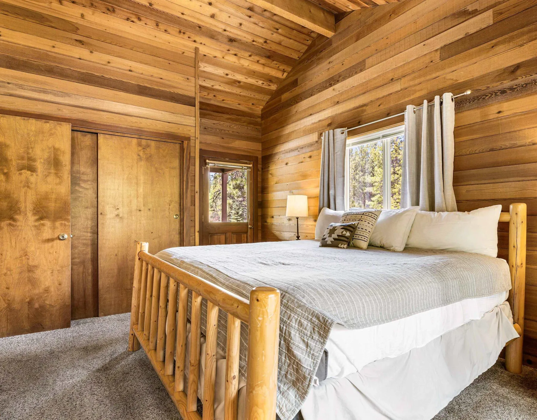 A bedroom with a large bed, wooden walls, and a window with curtains.