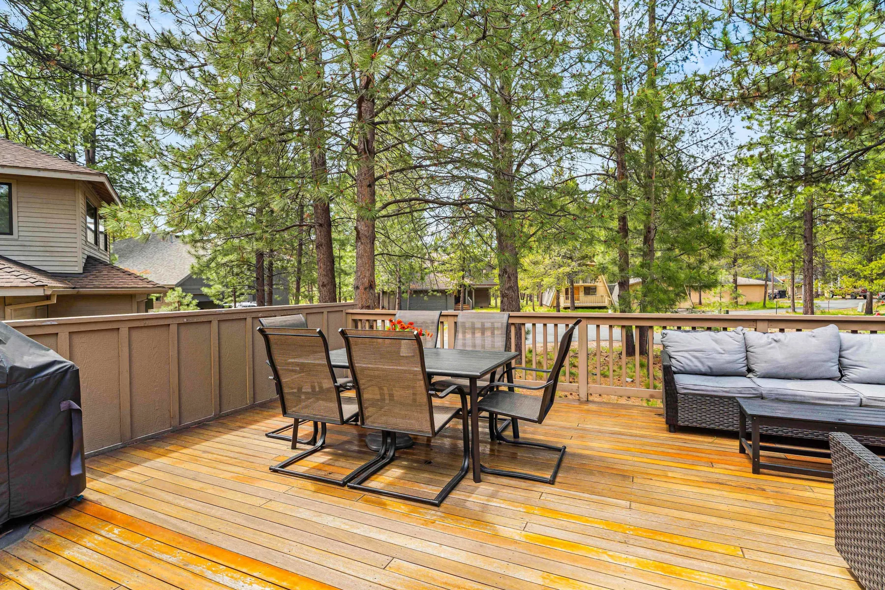 A wooden deck with a dining table and seating overlooks a wooded outdoor area.