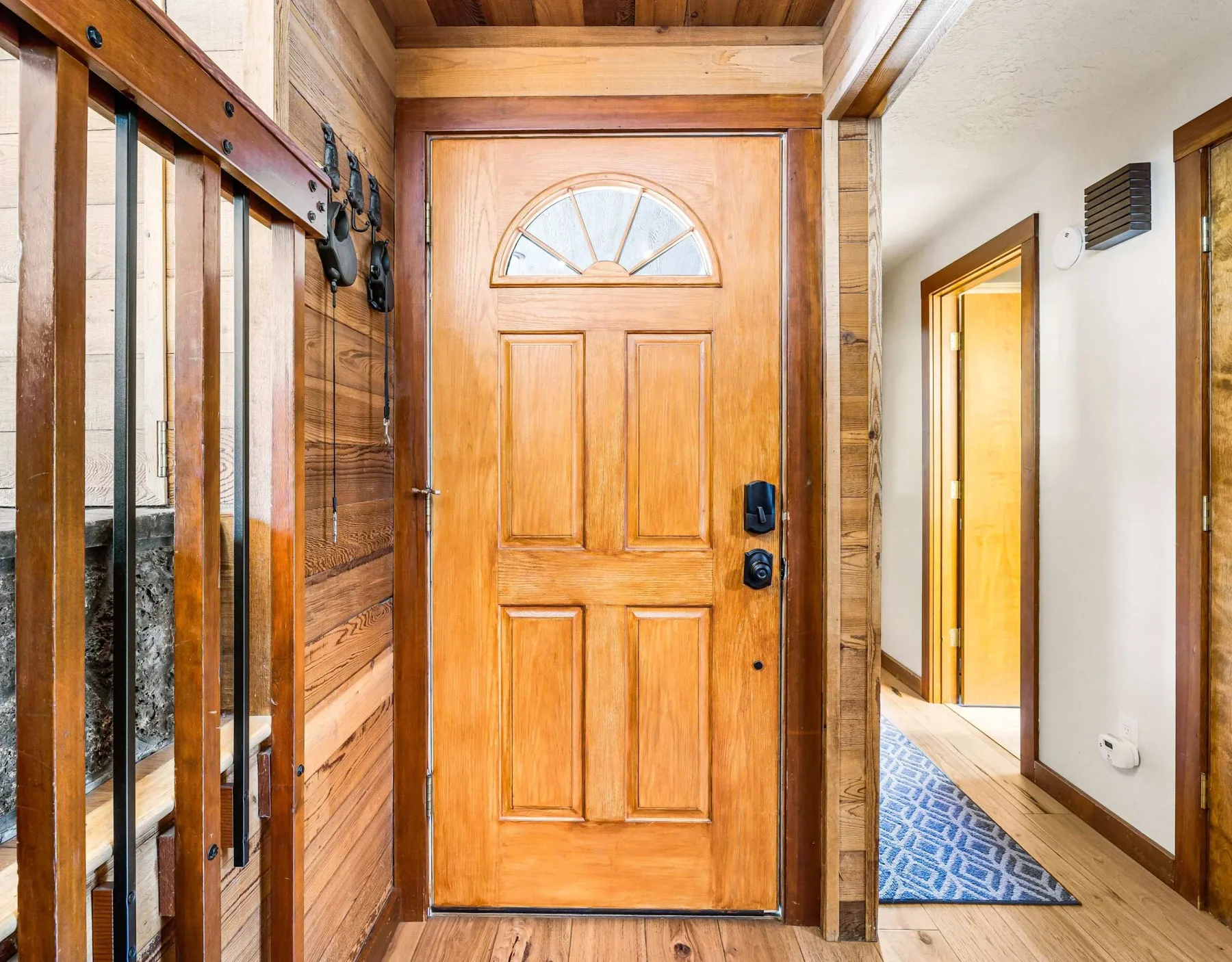 A wooden entry door opens onto a hallway with wood trim and a patterned runner.