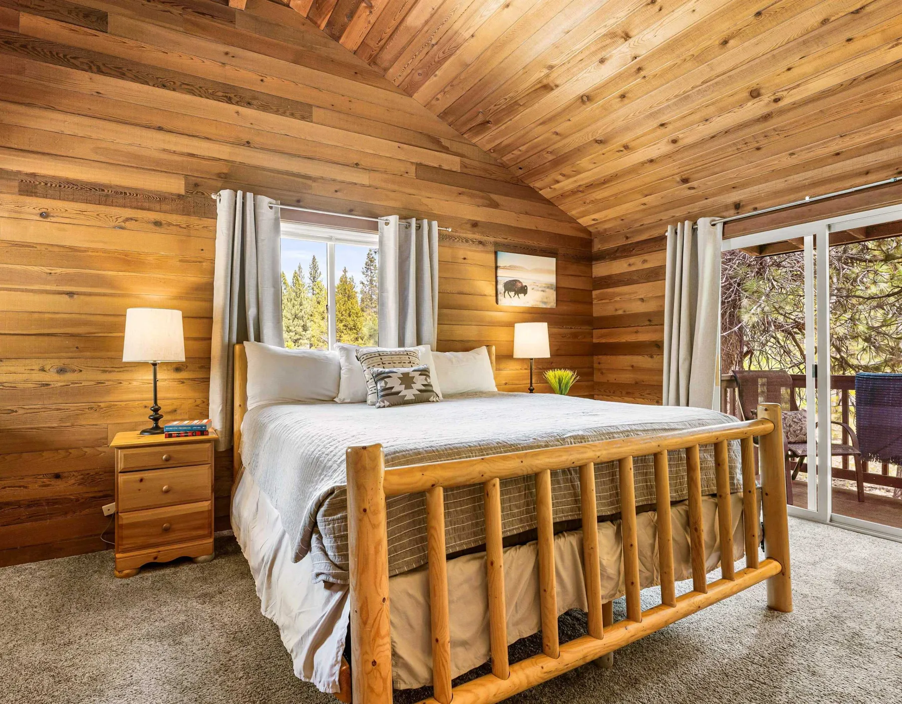 A bedroom with a large bed, bedside tables, and windows overlooking trees.