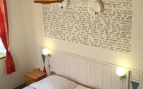 Representative hotel space: A bedroom with a bed, bedside table, and wall covered in printed text.