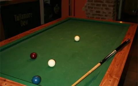 Representative hotel space: A billiards table with several balls and a cue in a dim room.