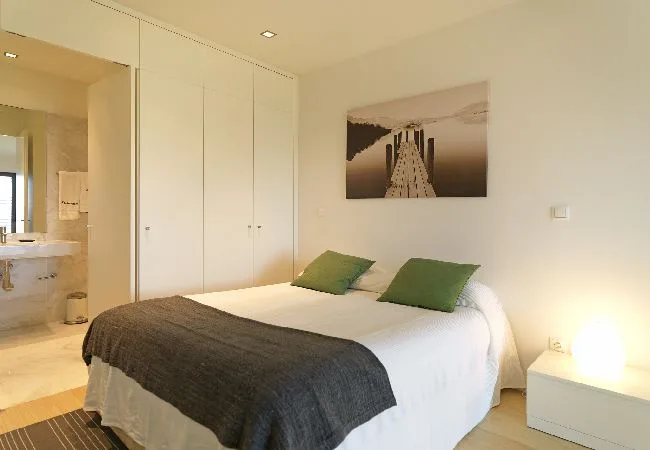 Un dormitorio con una cama doble, almohadas verdes y un cuadro en la pared.