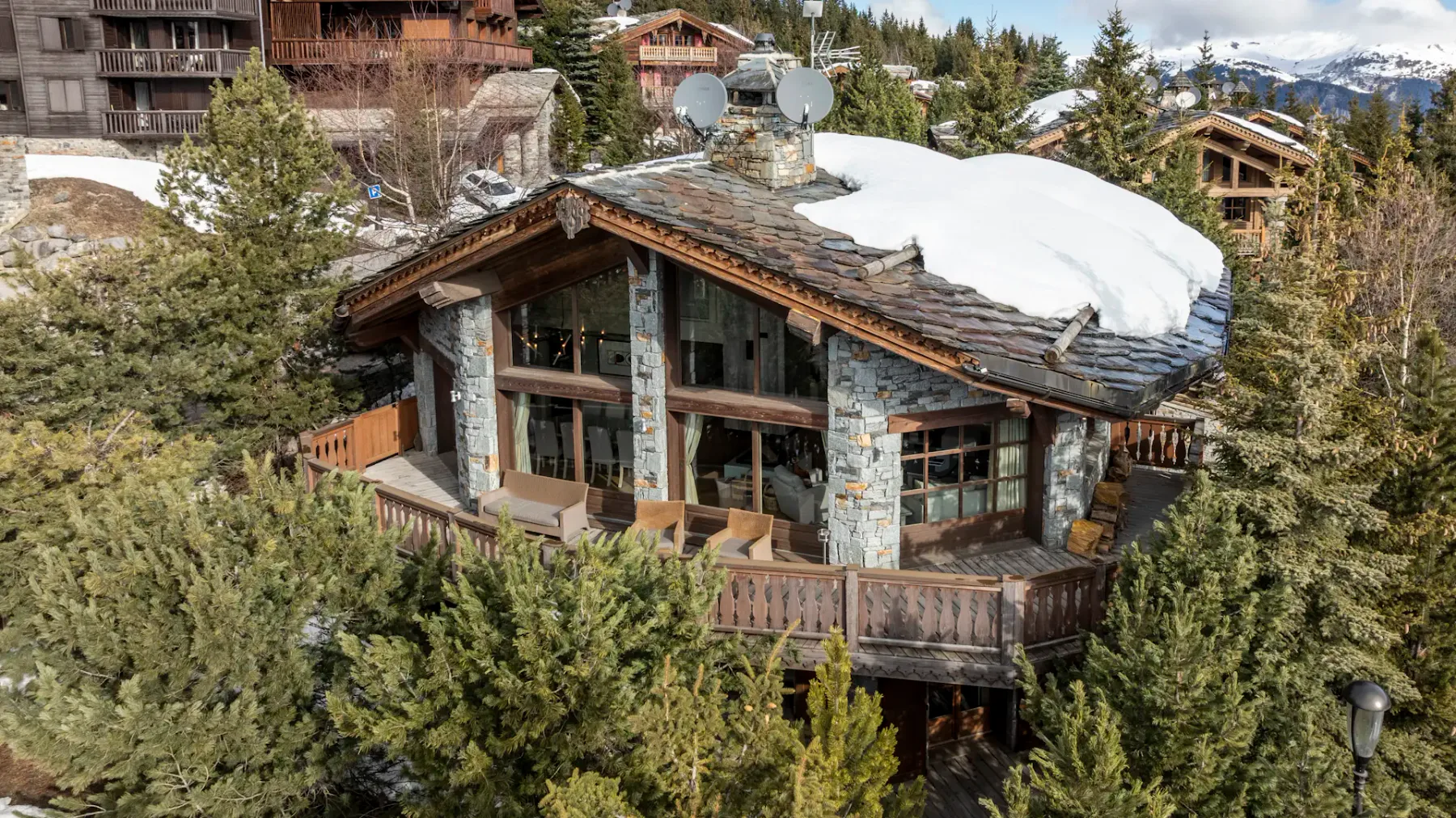 Un edificio de estilo chalet está rodeado de árboles de hoja perenne, con nieve en parte del techo.