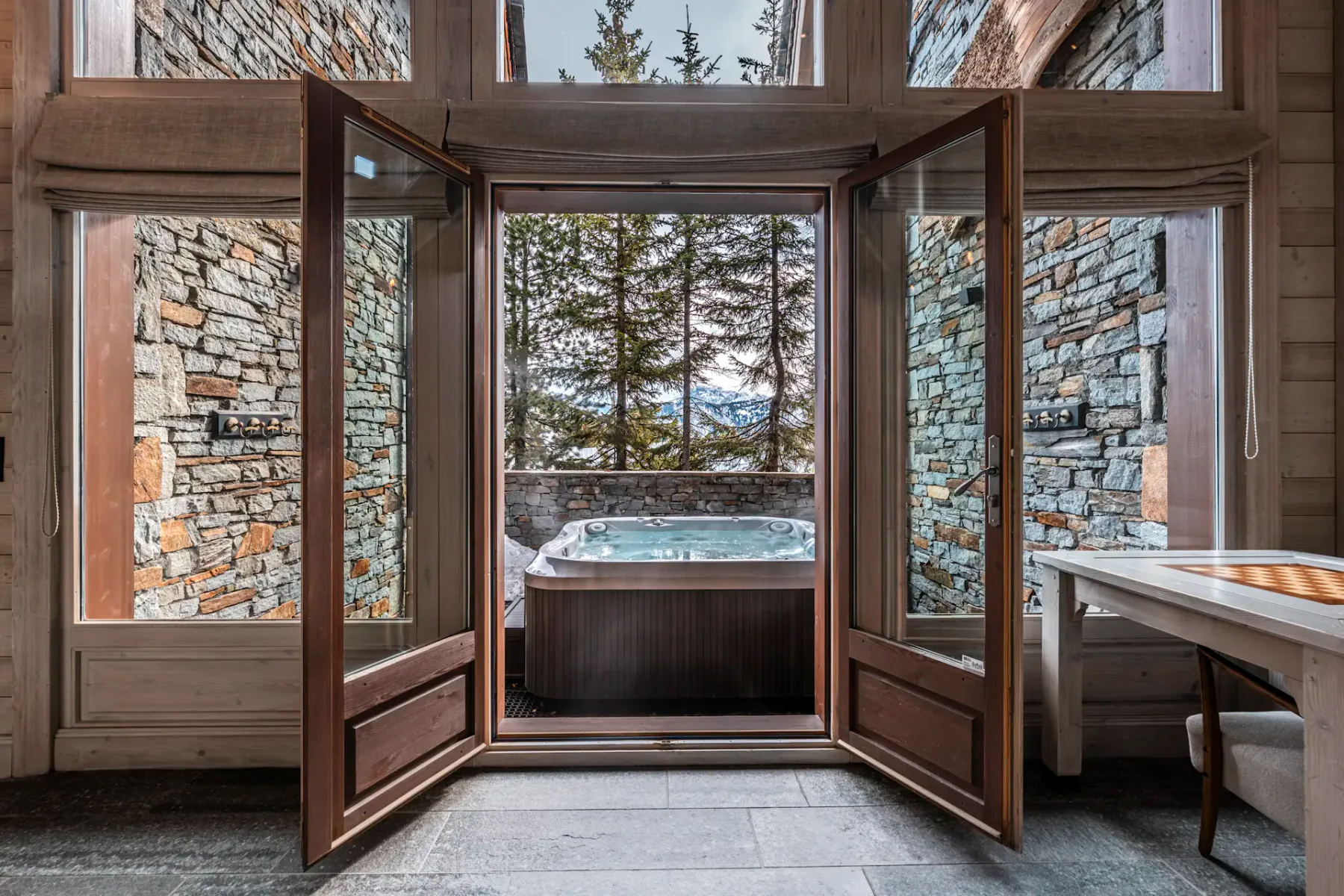 Una bañera de hidromasaje al aire libre queda enmarcada por puertas abiertas y paredes de piedra.