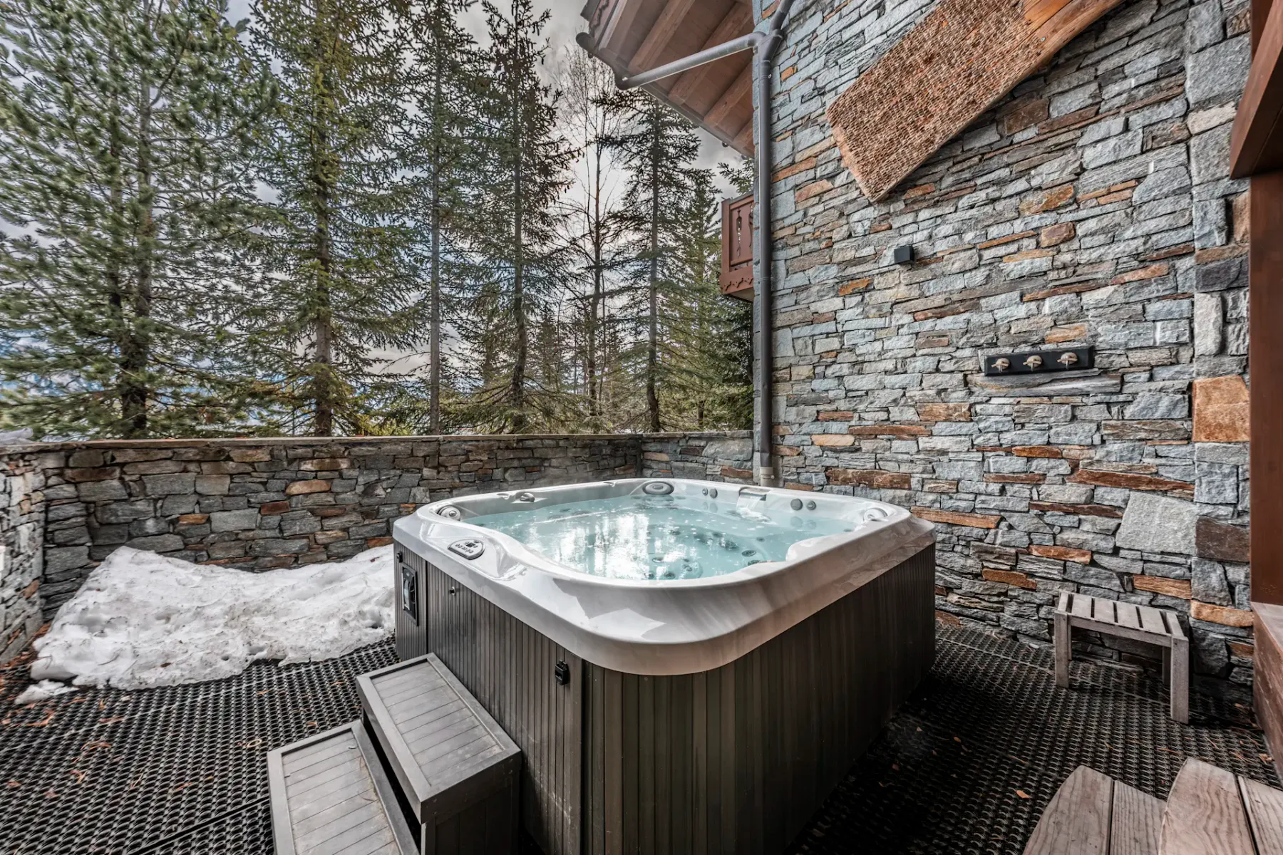 Una bañera de hidromasaje exterior está en una terraza de piedra rodeada de árboles.