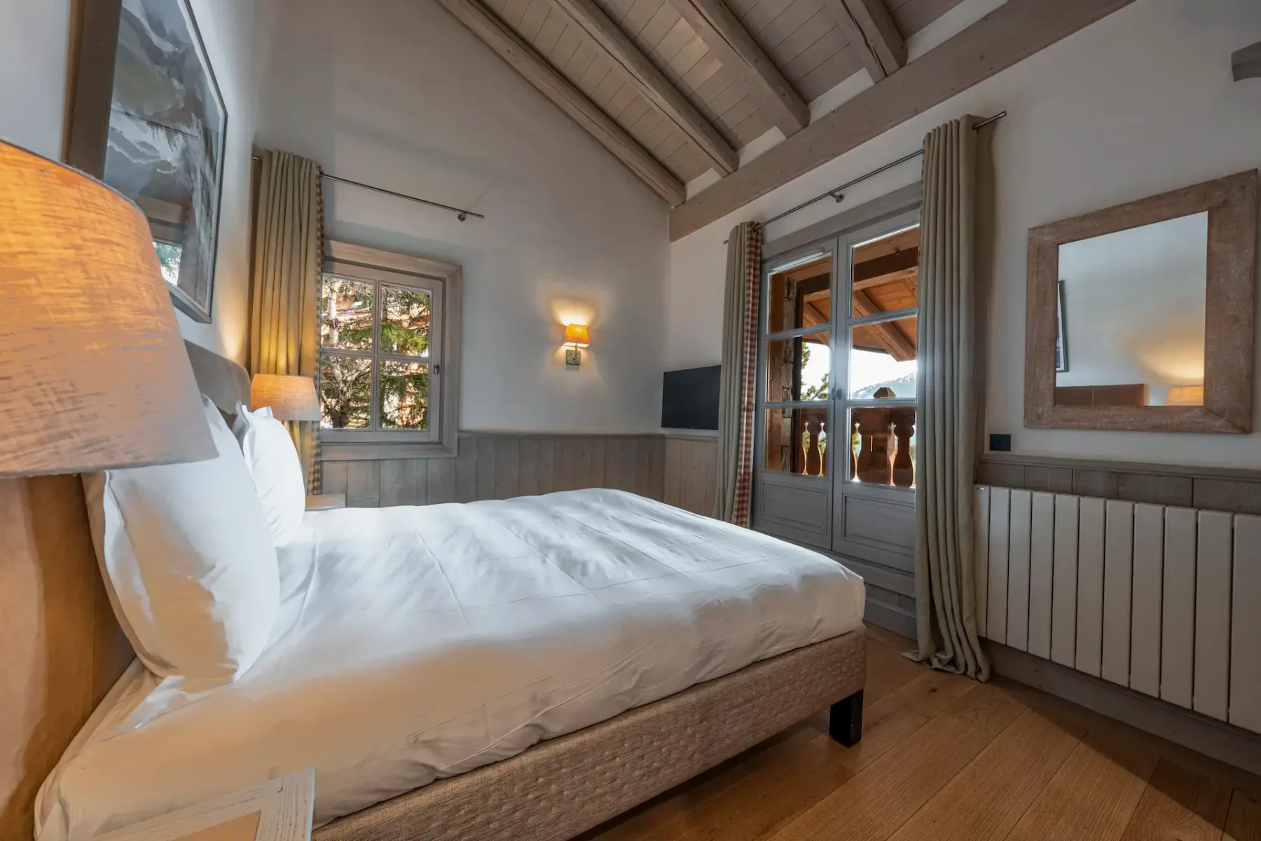 Un dormitorio con una cama, ventanas con cortinas y puertas de vidrio que dan a un balcón.