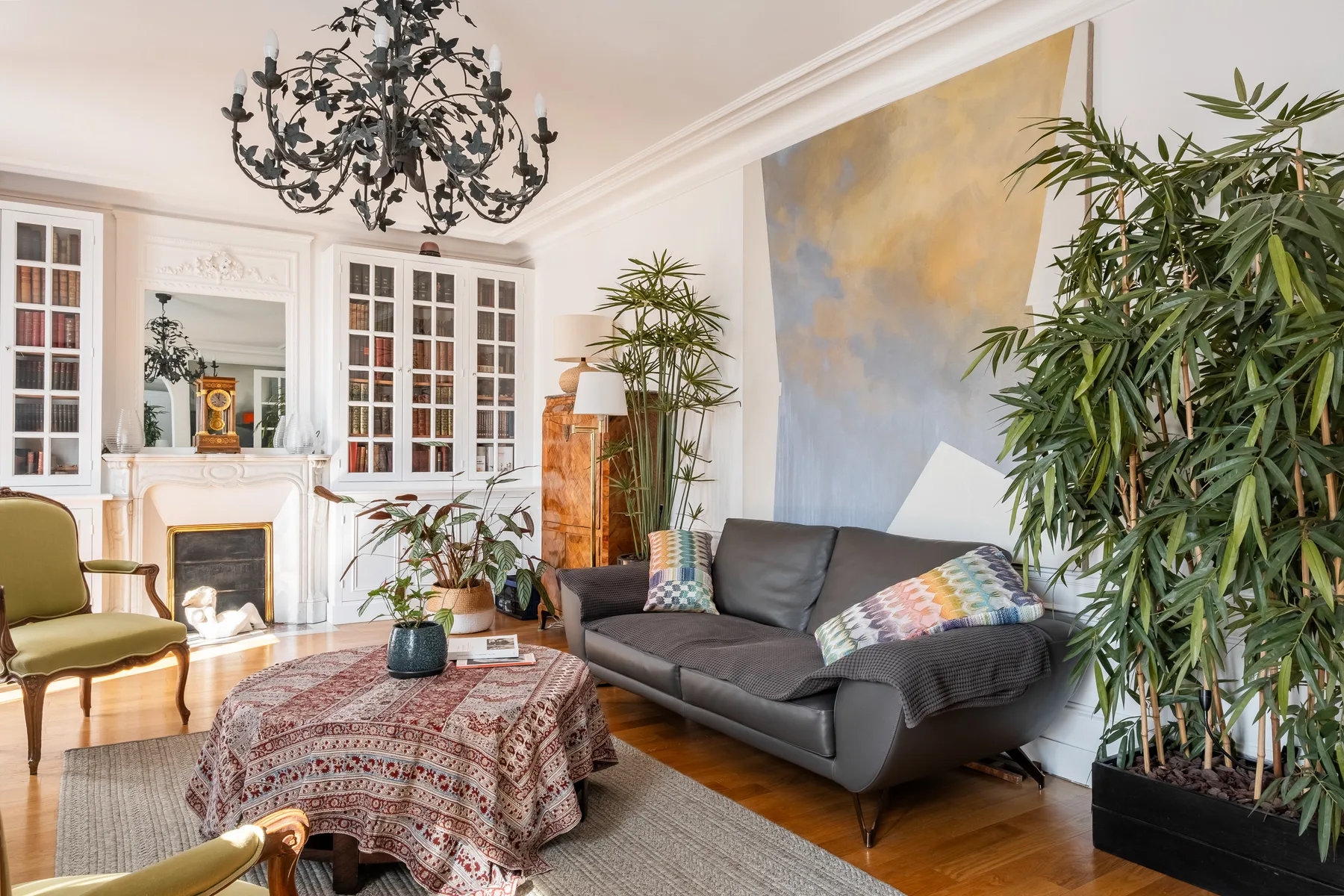 A bright living room with a gray sofa, fireplace, and large plants.