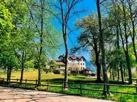 Representative hotel space: A large house stands among trees beside an open grassy lawn.