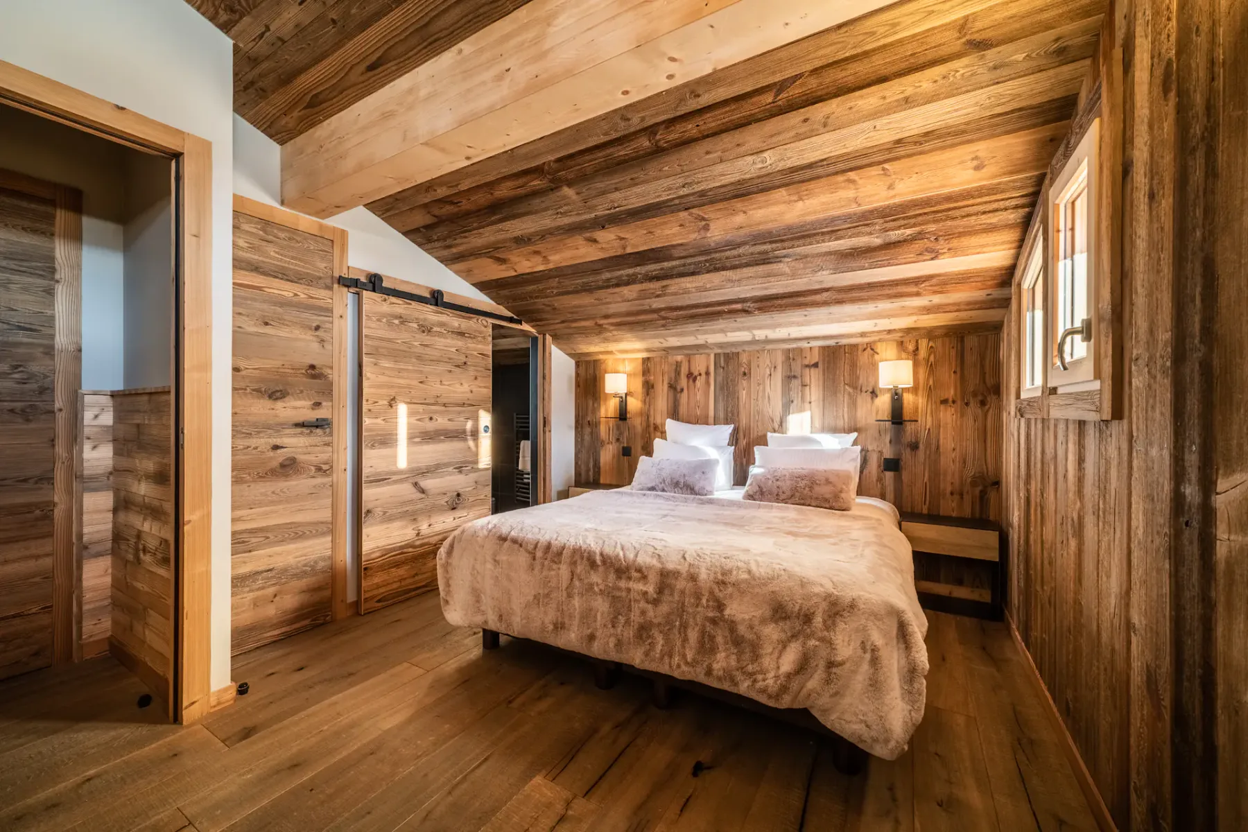Dormitorio revestido de madera con una cama bajo un techo inclinado de madera.