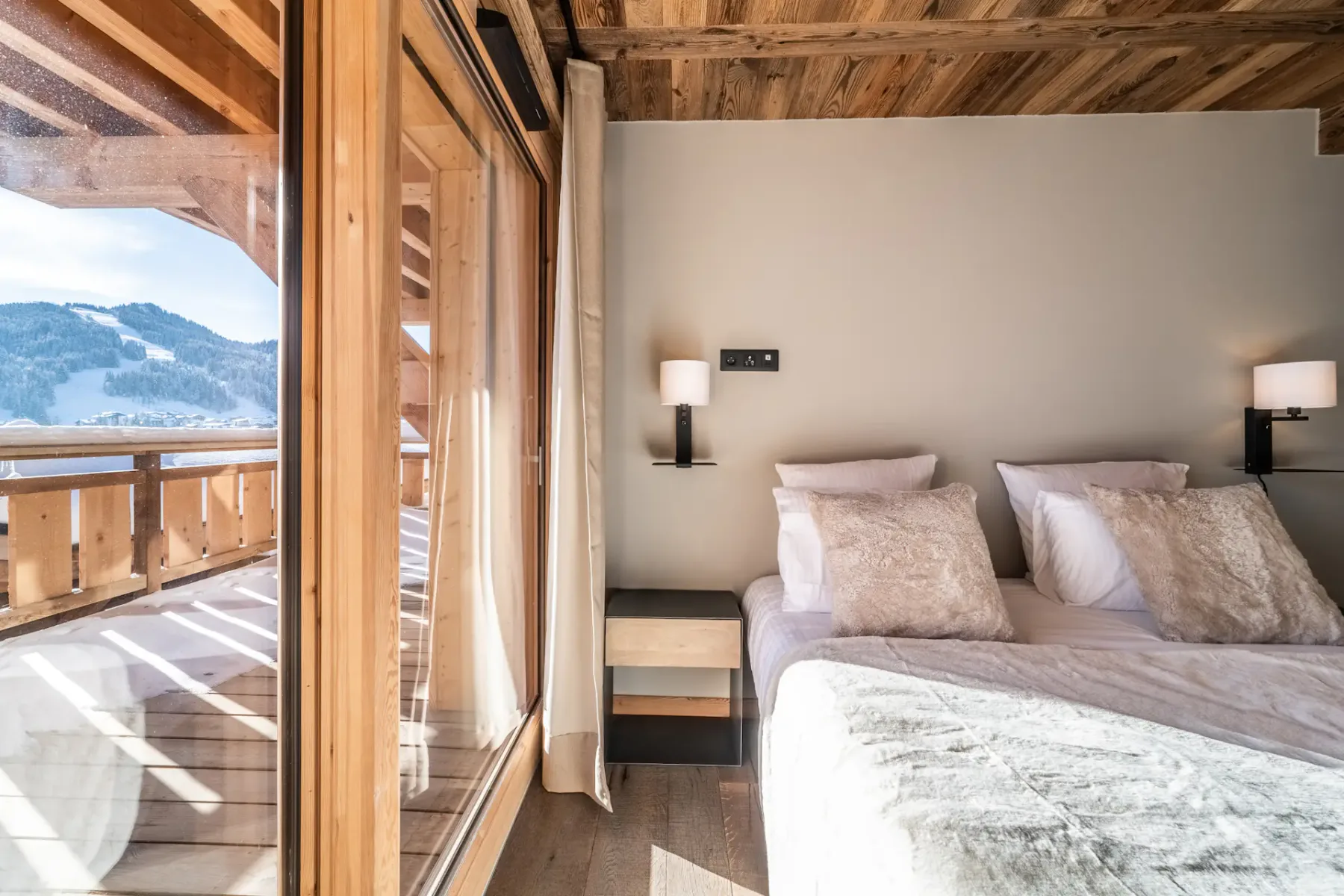 Un dormitorio con una cama junto a grandes ventanales con vistas a un paisaje montañoso nevado.