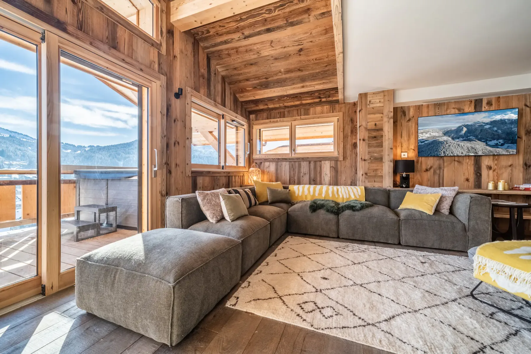 Una sala revestida de madera con asientos seccionales y grandes ventanales con vistas a las montañas.