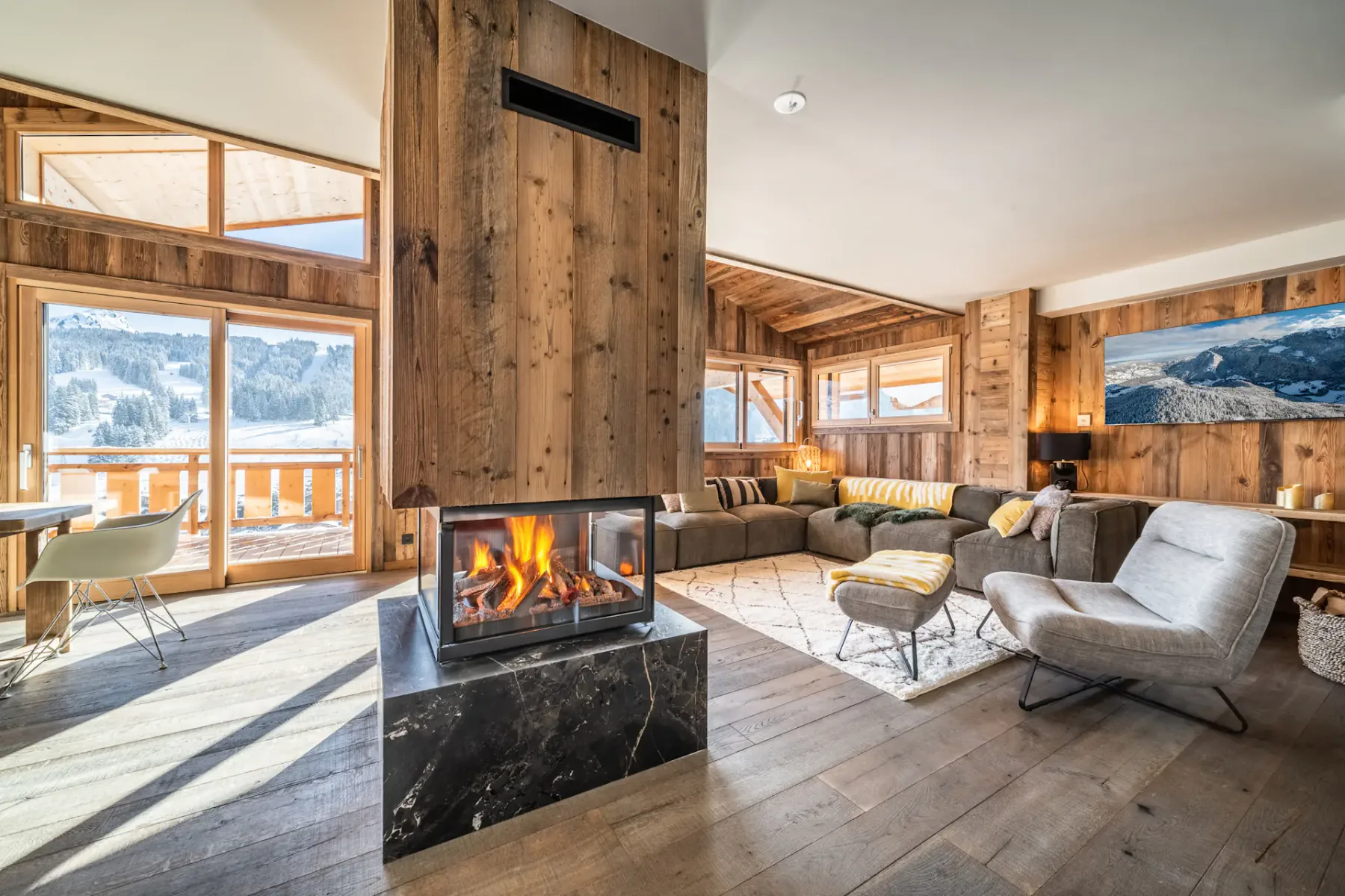 Una sala luminosa con chimenea, asientos y grandes ventanas con vistas a montañas nevadas.
