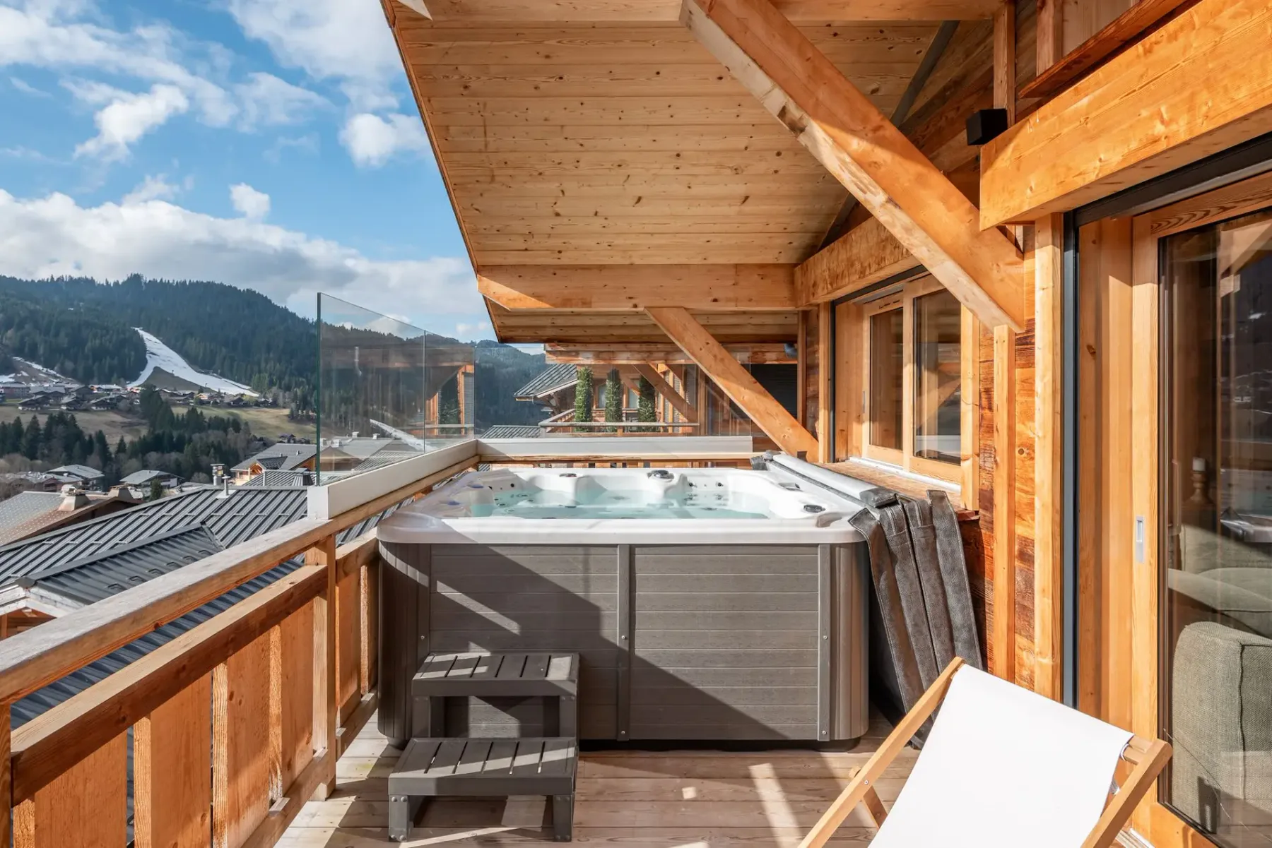 Una bañera de hidromasaje está en un balcón de madera con vistas a un paisaje montañoso.