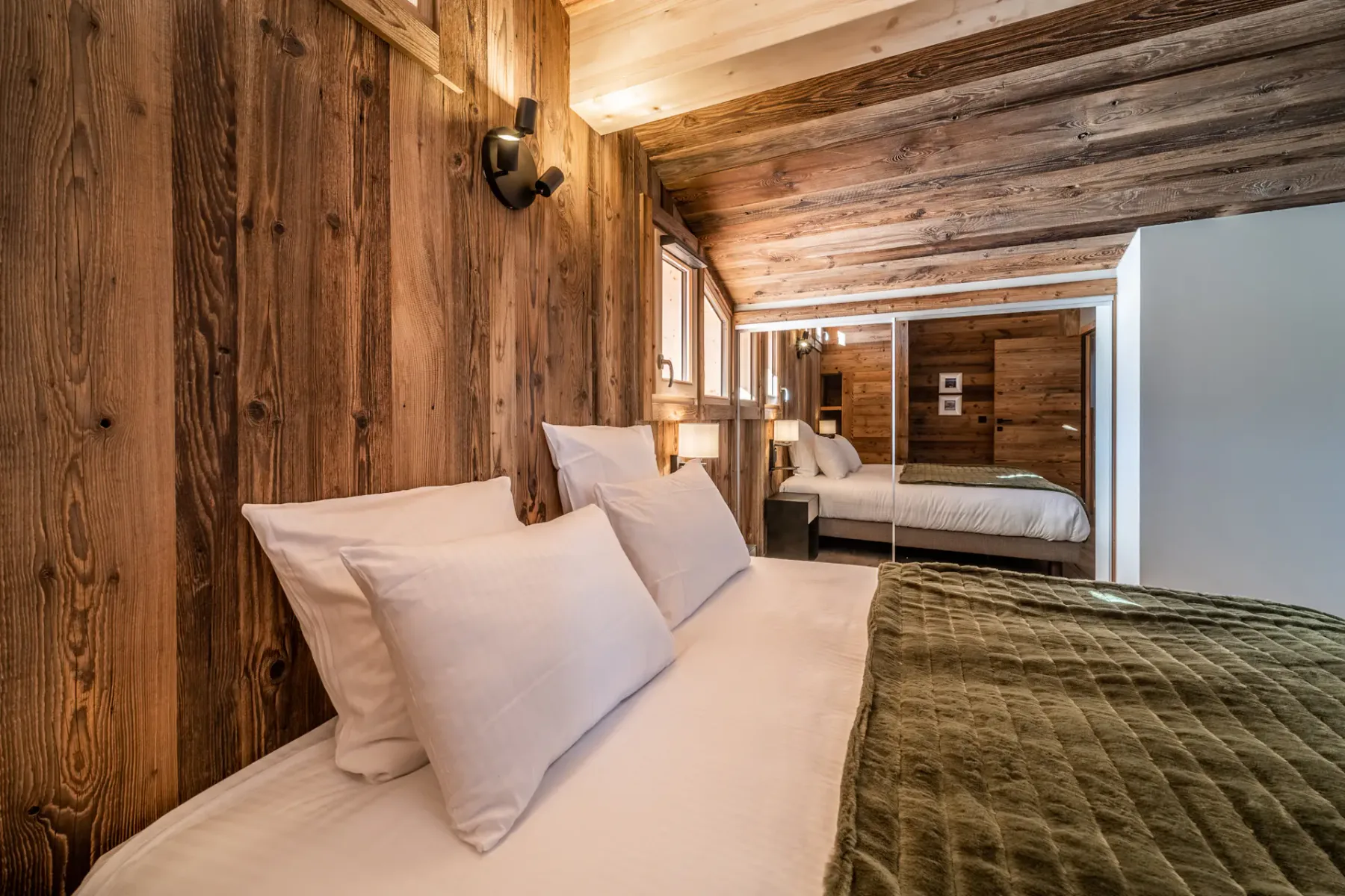 Un dormitorio con ropa de cama blanca, una colcha verde y paredes revestidas de madera.