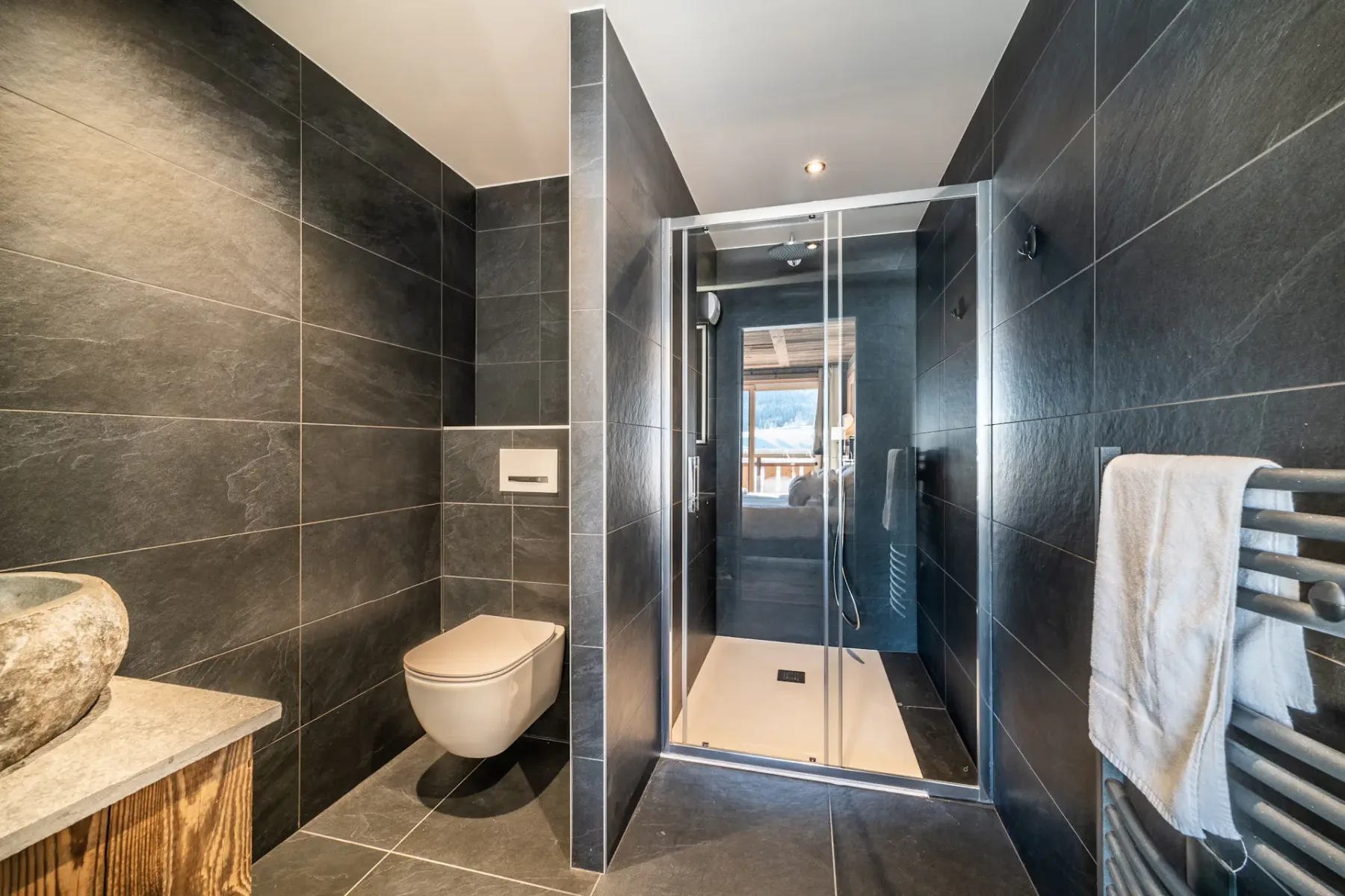 Un baño moderno con ducha de vidrio y paredes de azulejos oscuros.