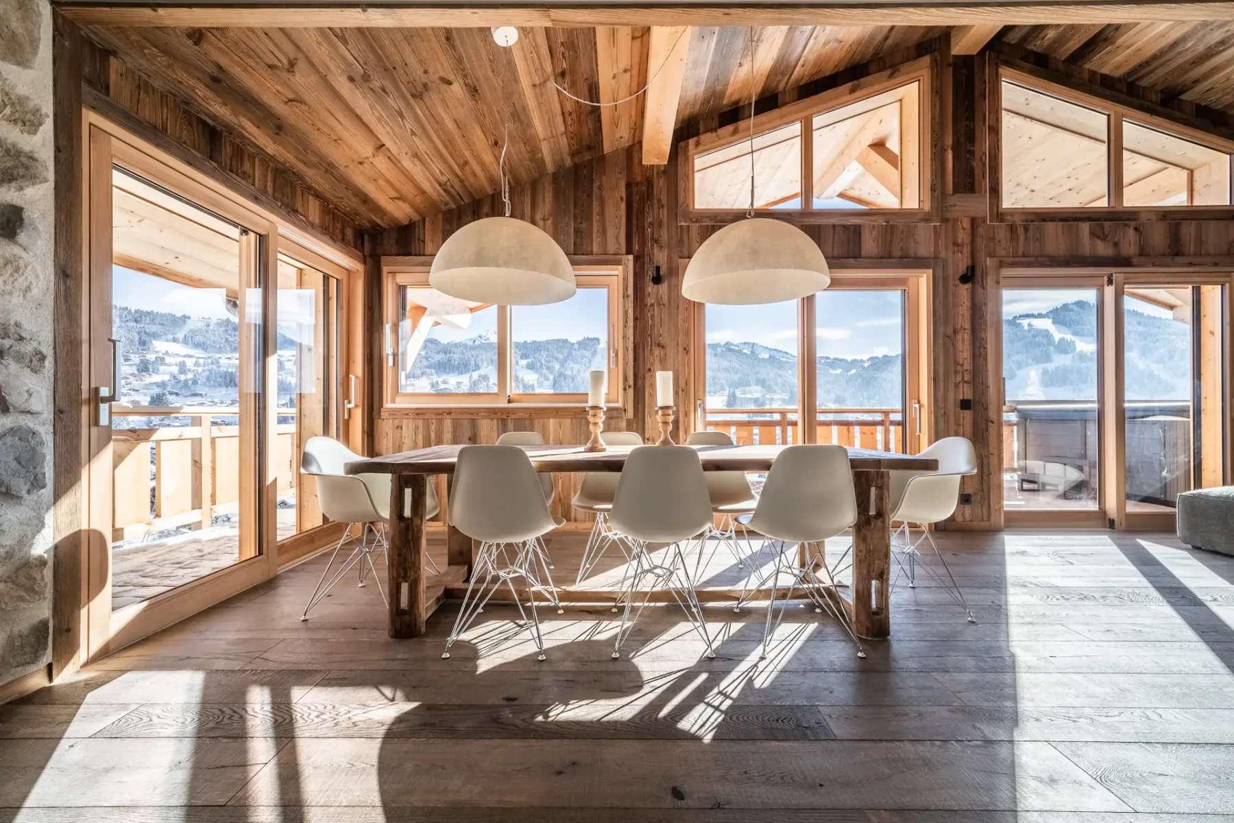 Comedor revestido de madera con una mesa larga, sillas y vistas a las montañas por grandes ventanales.