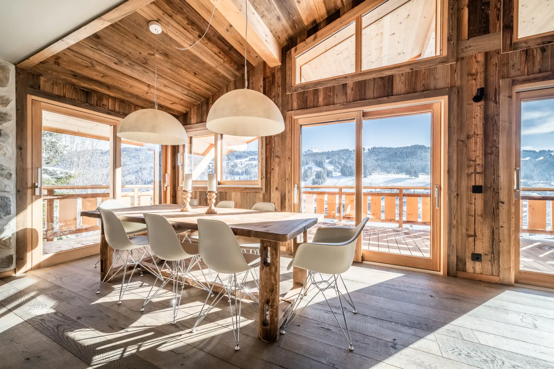Un comedor revestido de madera con una mesa larga y grandes ventanas con vistas a las montañas.