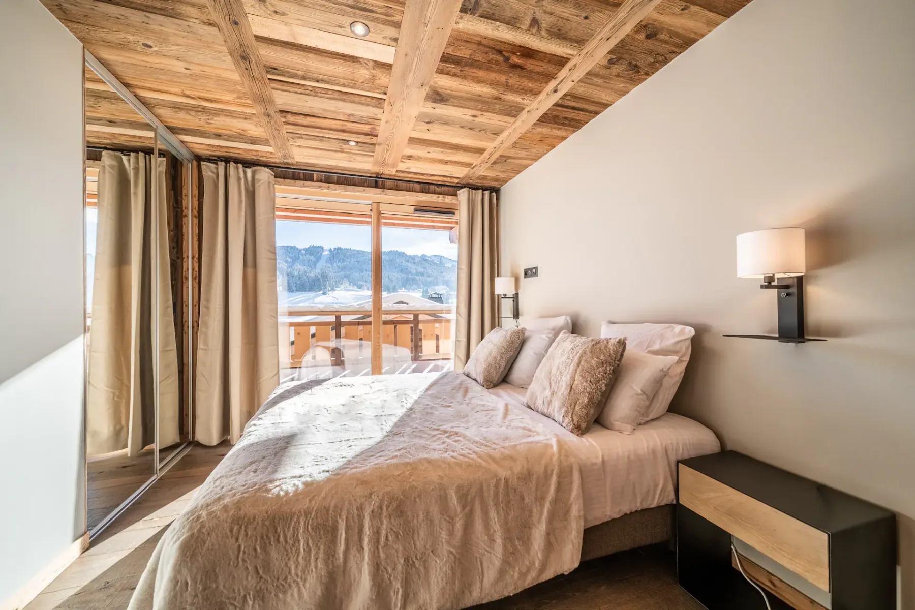 Un dormitorio con una cama junto a una gran ventana con vistas a las montañas.