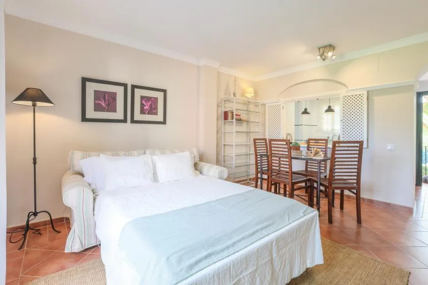 A bedroom with a white bed and a dining table behind it.