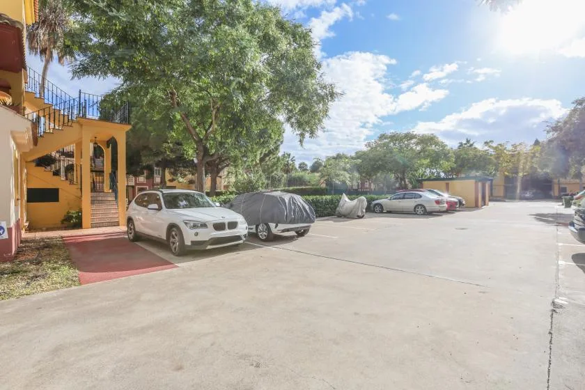 Shared amenity: A paved parking area with several cars beside a building and trees.