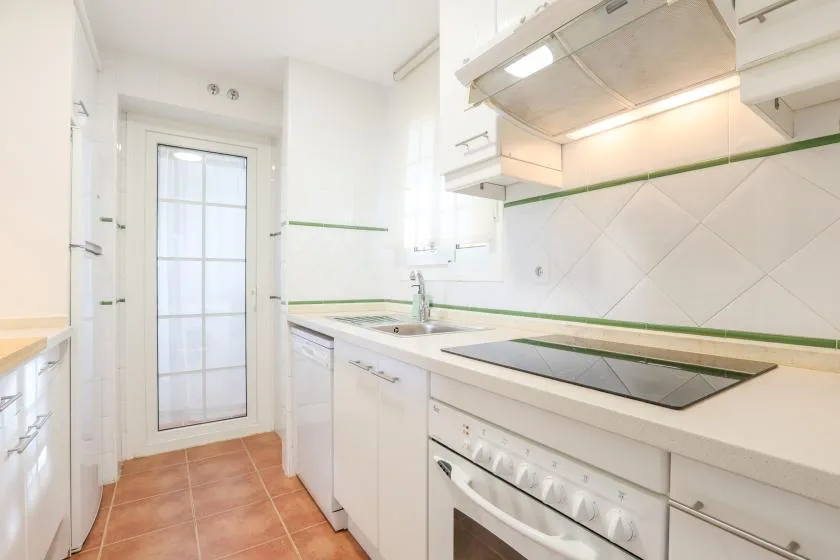 A bright kitchen with white cabinets and a cooktop along the counter.