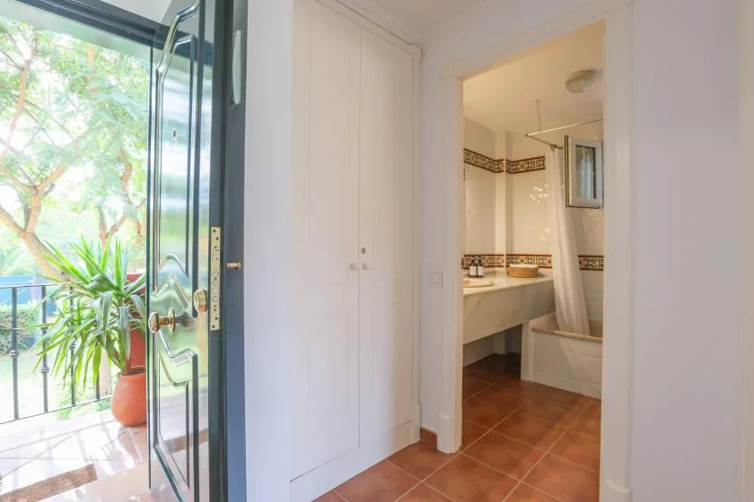 A bathroom is visible through the doorway beside an open glass door to a balcony.