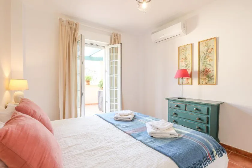 A bedroom with a bed, teal dresser, and open balcony doors.