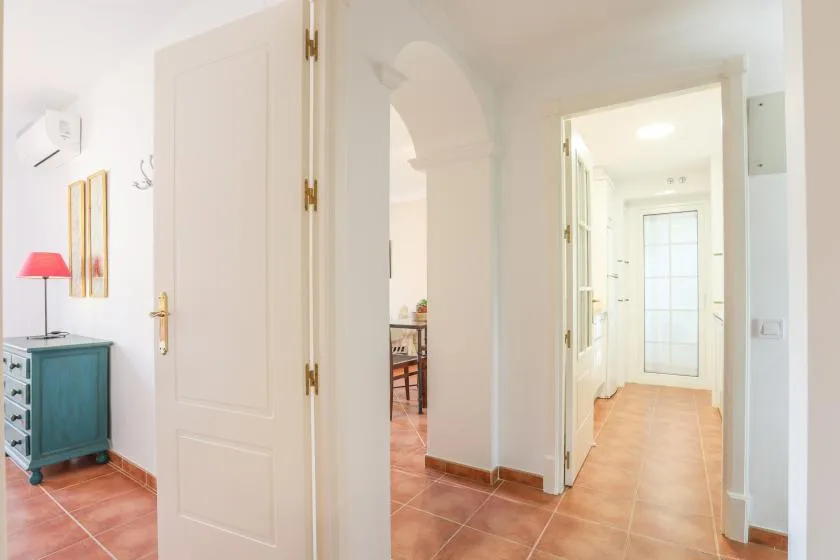 A bright interior hallway with terracotta-colored tile and open doorways.