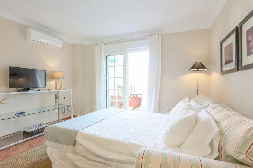 A bright bedroom with a neatly made bed and glass doors opening onto a balcony.