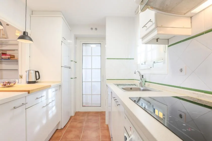 A bright kitchen with white cabinets, a tiled floor, and a glass-paneled door.