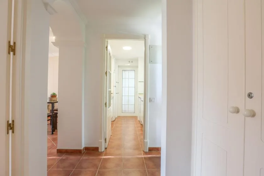 A hallway with terracotta-colored floor tiles and white doors.