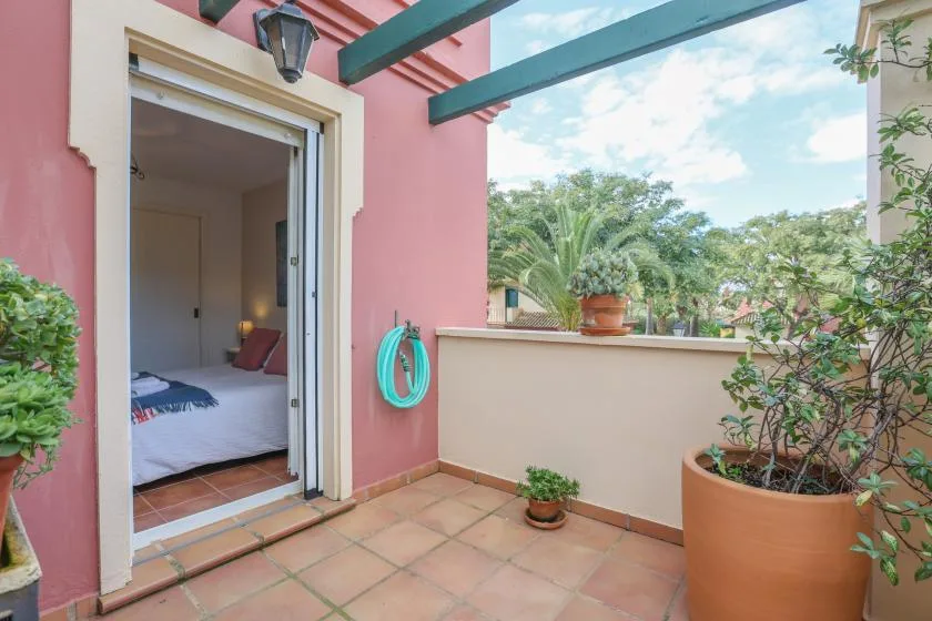 A tiled terrace beside an open bedroom doorway, with potted plants and a garden view.
