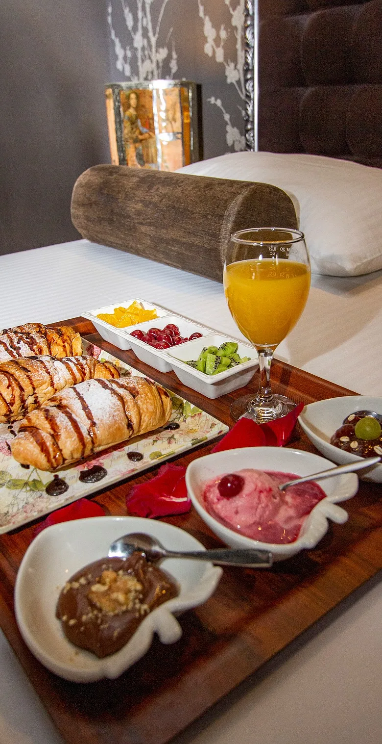 Espacio representativo del hotel: Una cama con una bandeja de desayuno que muestra pasteles, fruta y jugo.