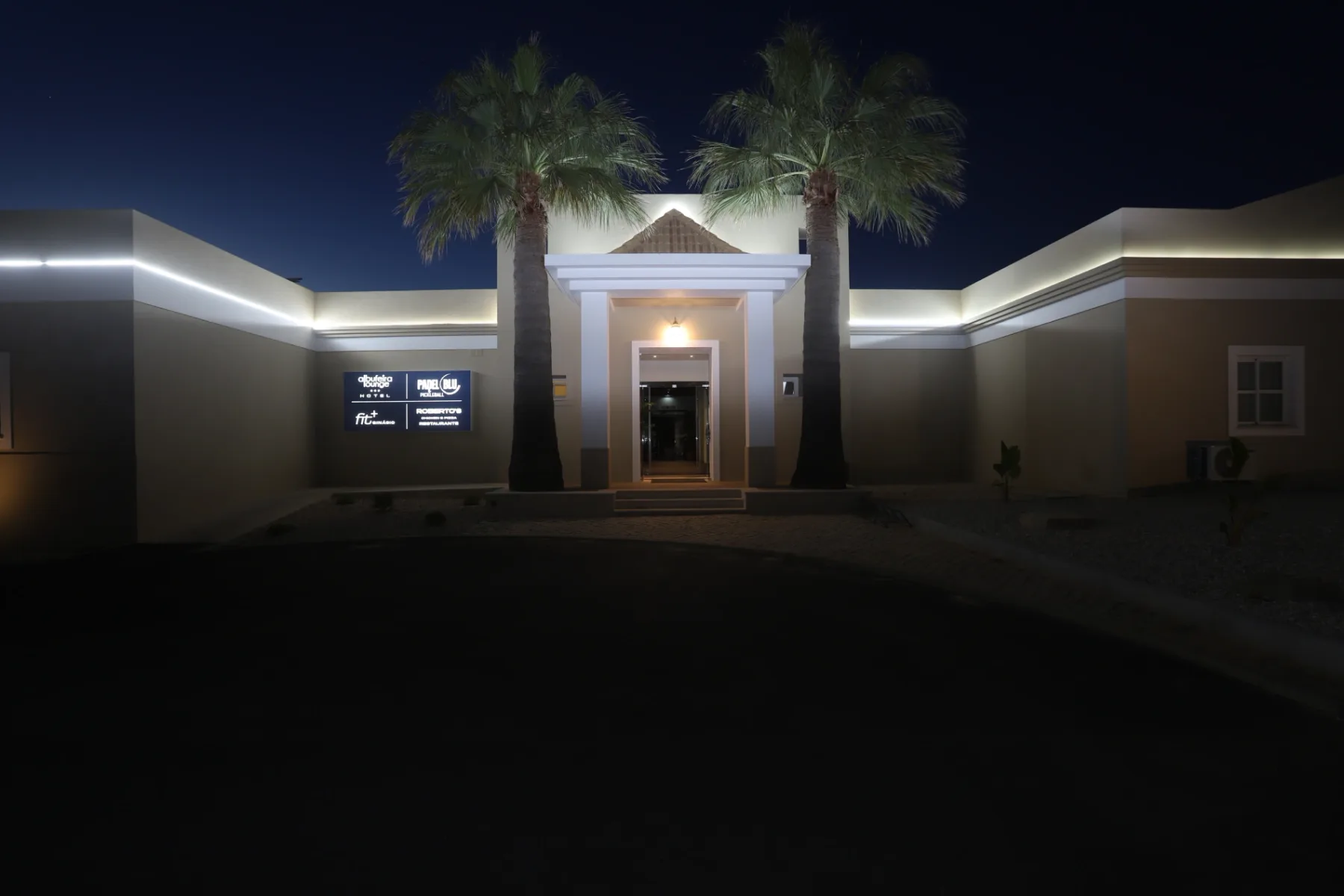 Representative hotel space: A building entrance at night is framed by palm trees and illuminated roofline lights.