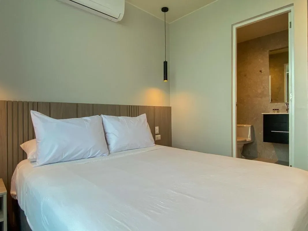 A bedroom with a neatly made bed and an open doorway to the bathroom.