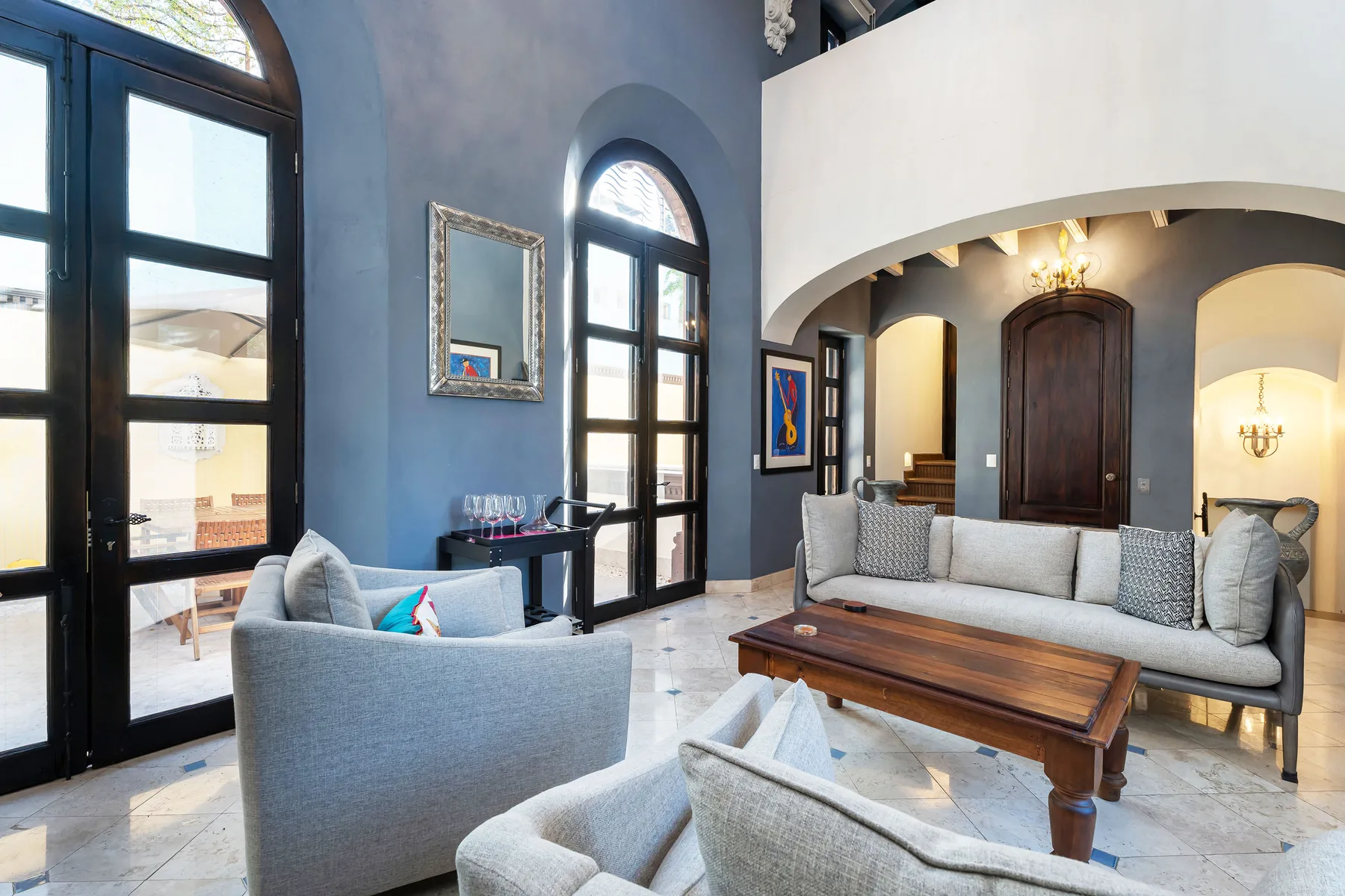 A spacious living room with gray seating, tall arched windows, and a wooden coffee table.