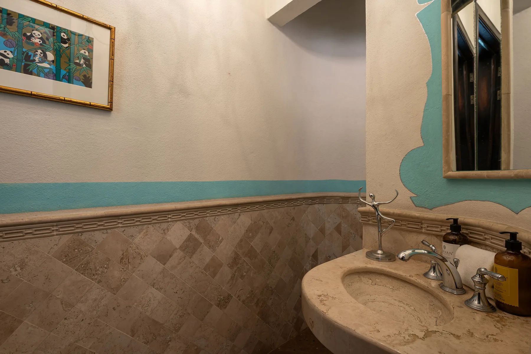 A bathroom sink sits beneath a mirror against a tiled wall.