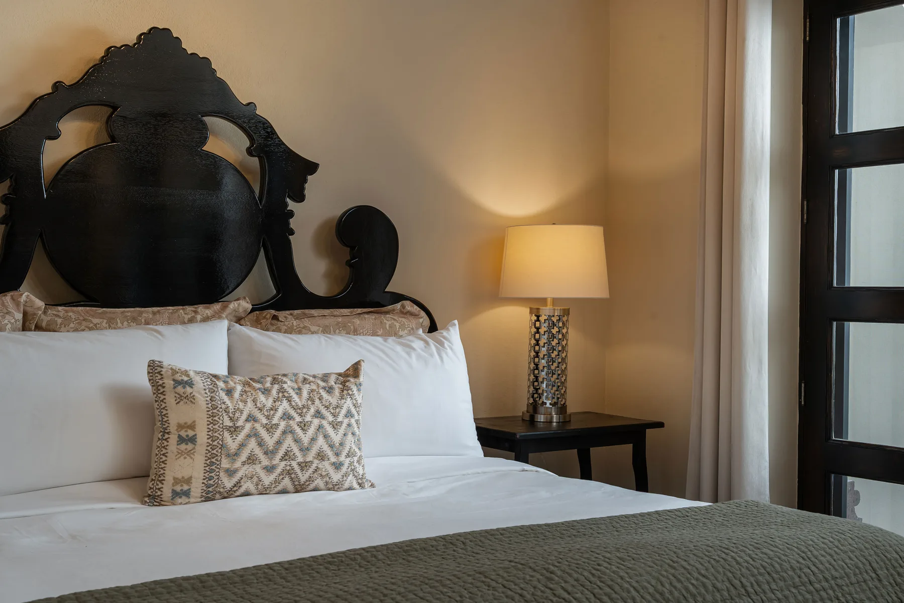 A bedroom with a neatly made bed and a lamp on a bedside table.
