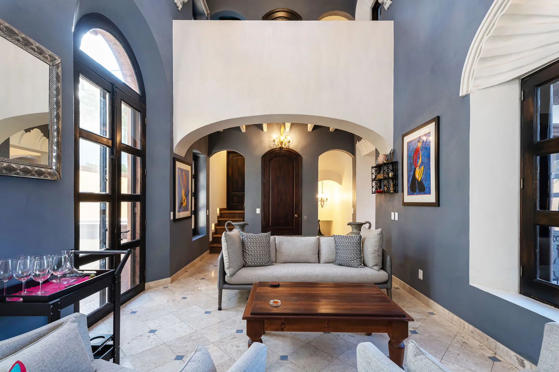 A living room with seating and a wooden coffee table beneath a high arch.