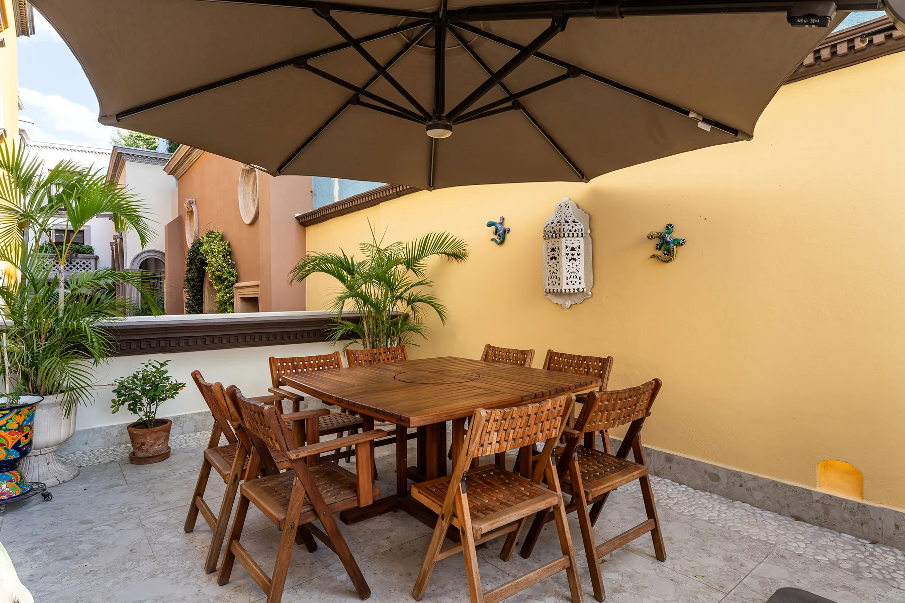 An outdoor dining area with a wooden table and seating beneath a large umbrella.