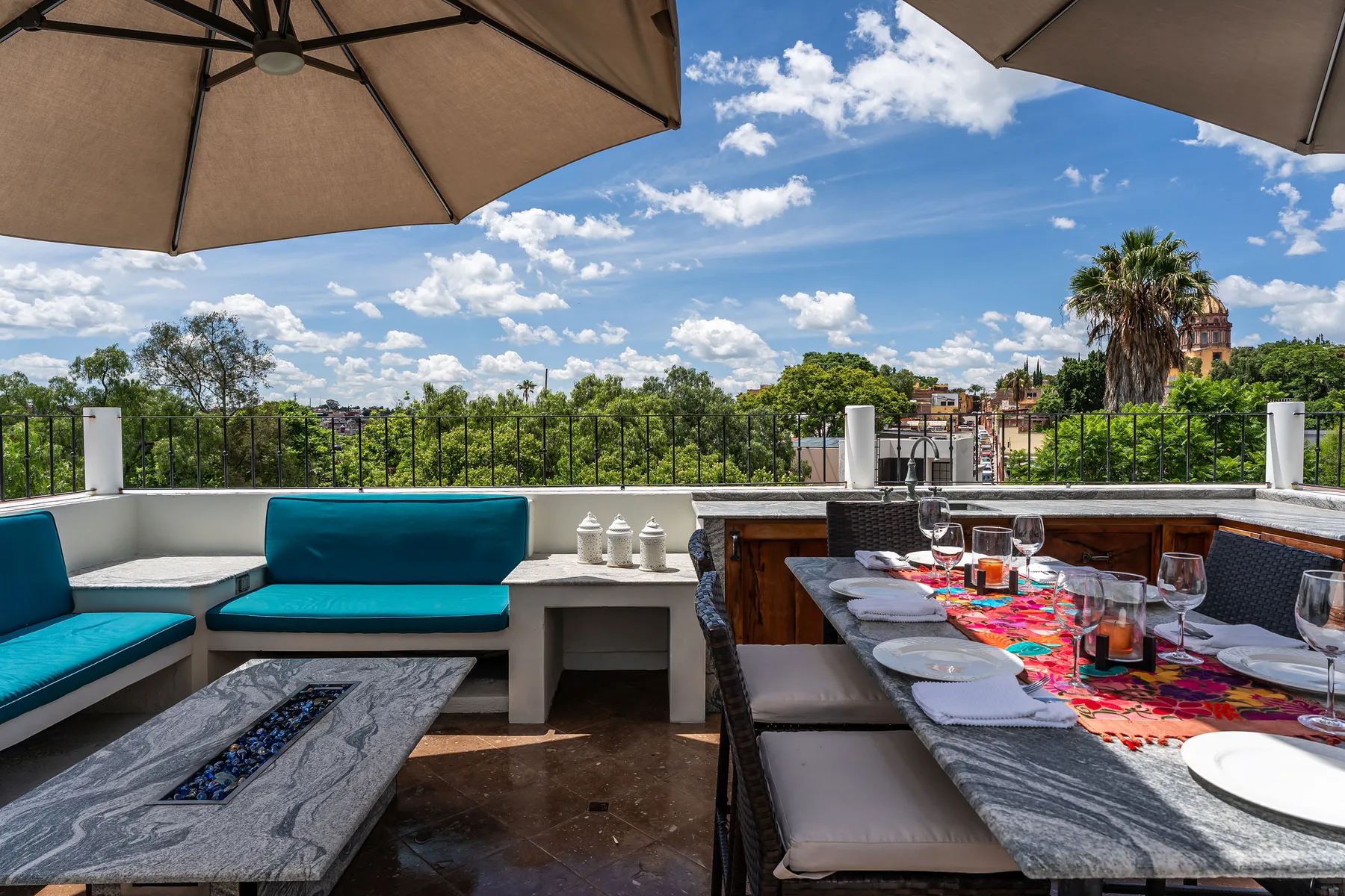 A rooftop terrace has outdoor seating and a dining table beneath umbrellas.