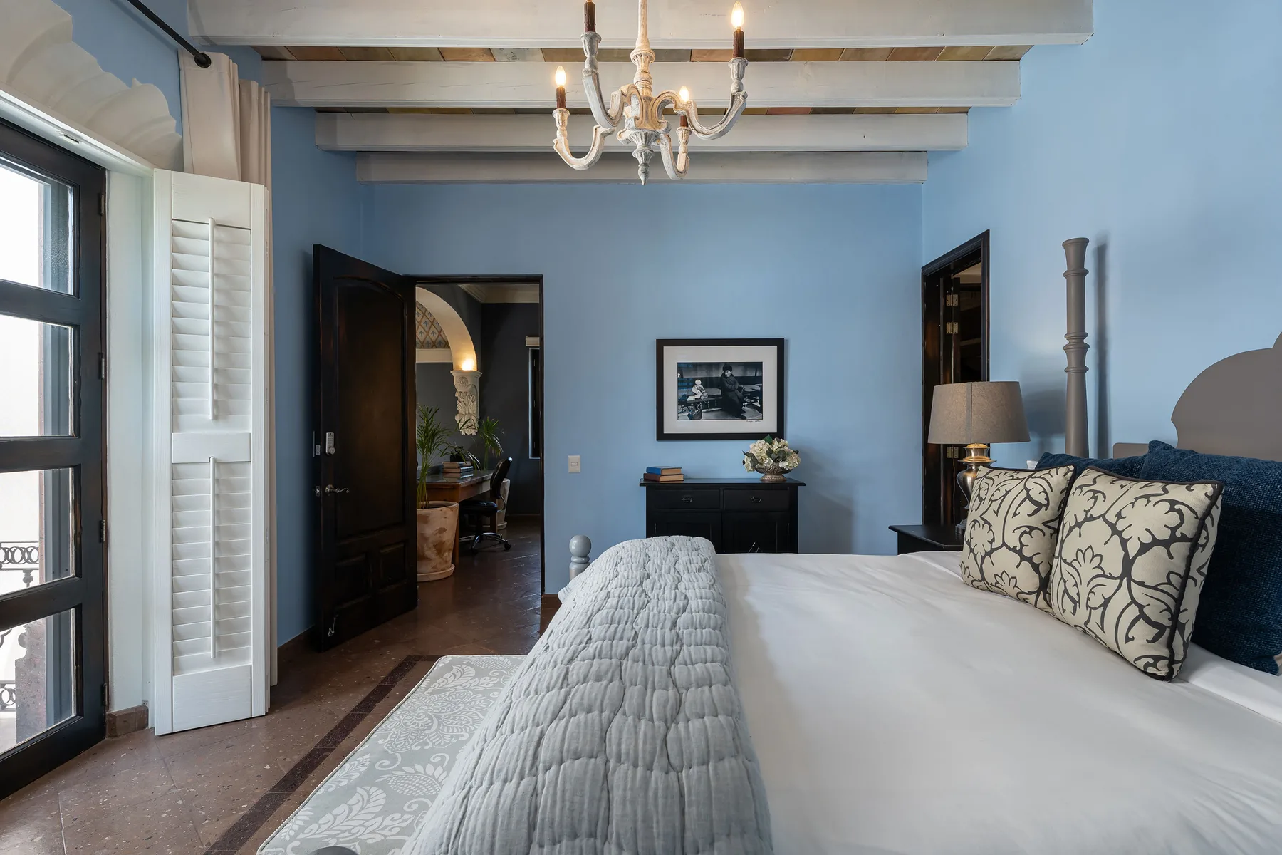 A bedroom with a neatly made bed, blue walls, and exposed ceiling beams.