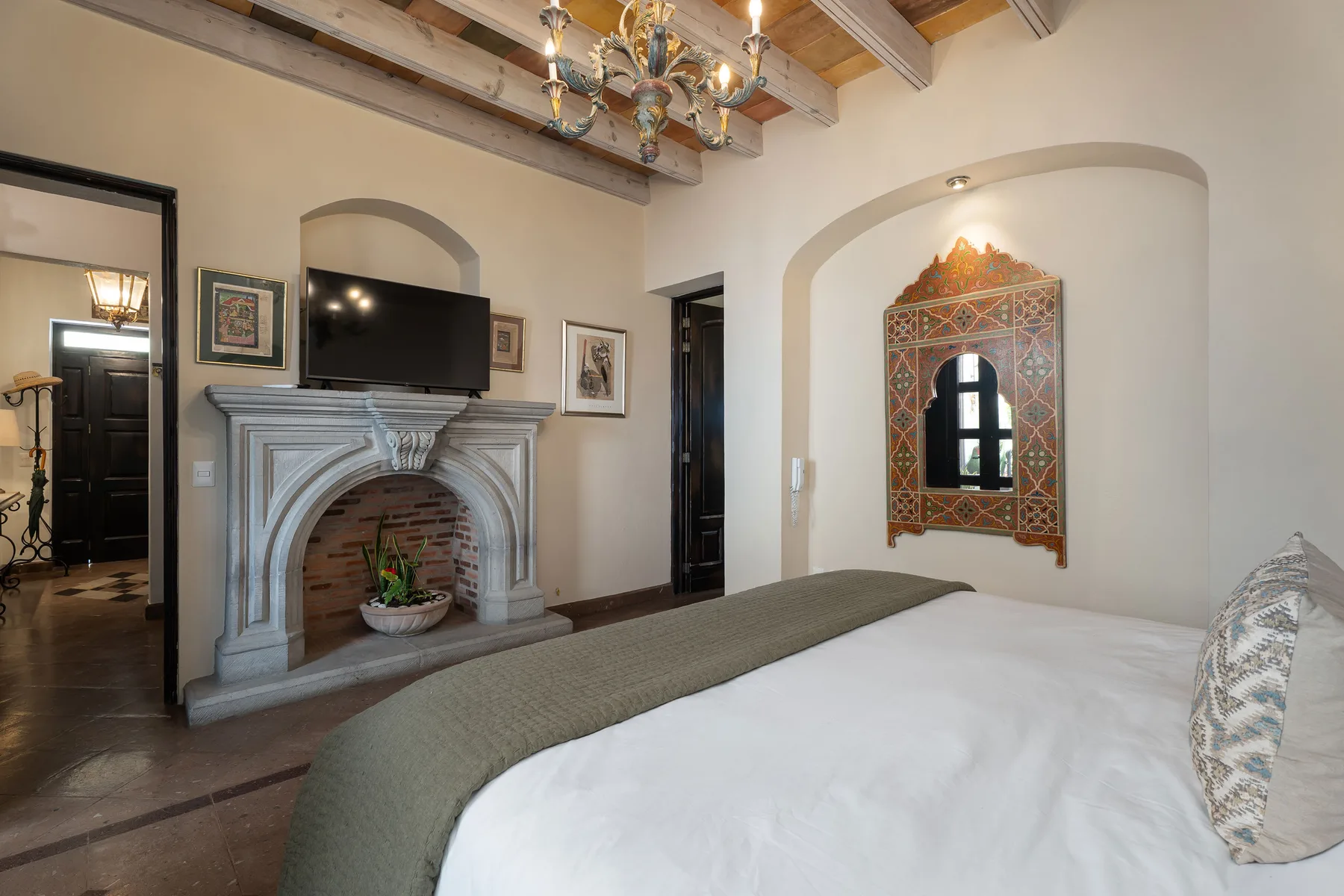 A bedroom with a bed, ornate fireplace, and decorative wall mirror.