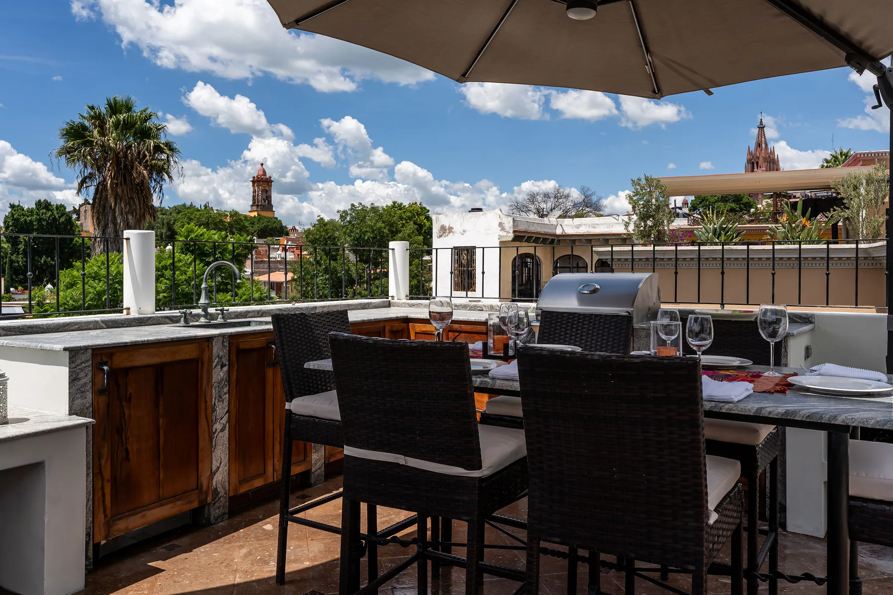 A rooftop dining terrace has an outdoor table and seating beneath a large umbrella.