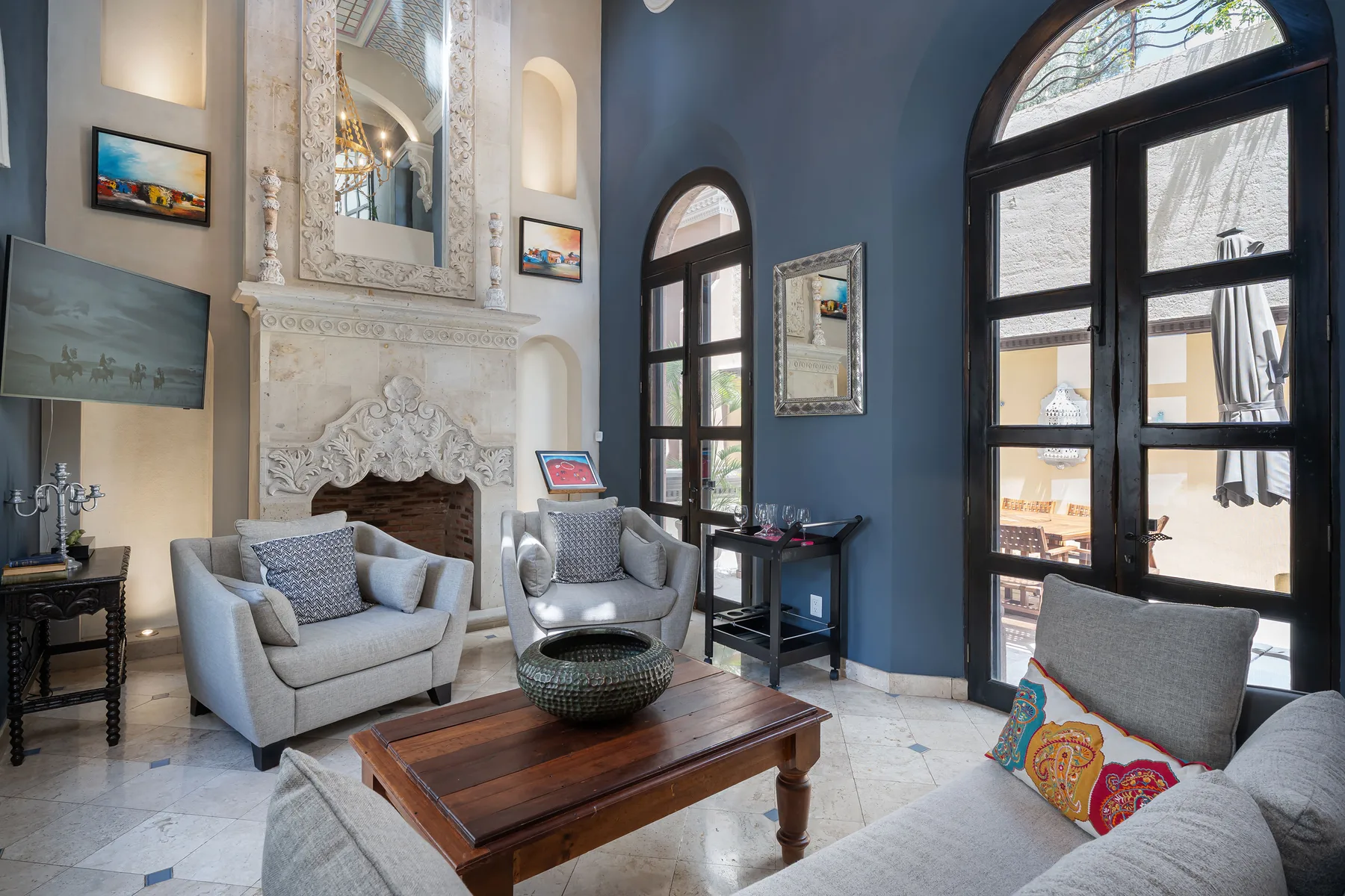 A living room with seating around a wooden coffee table beside tall arched windows.