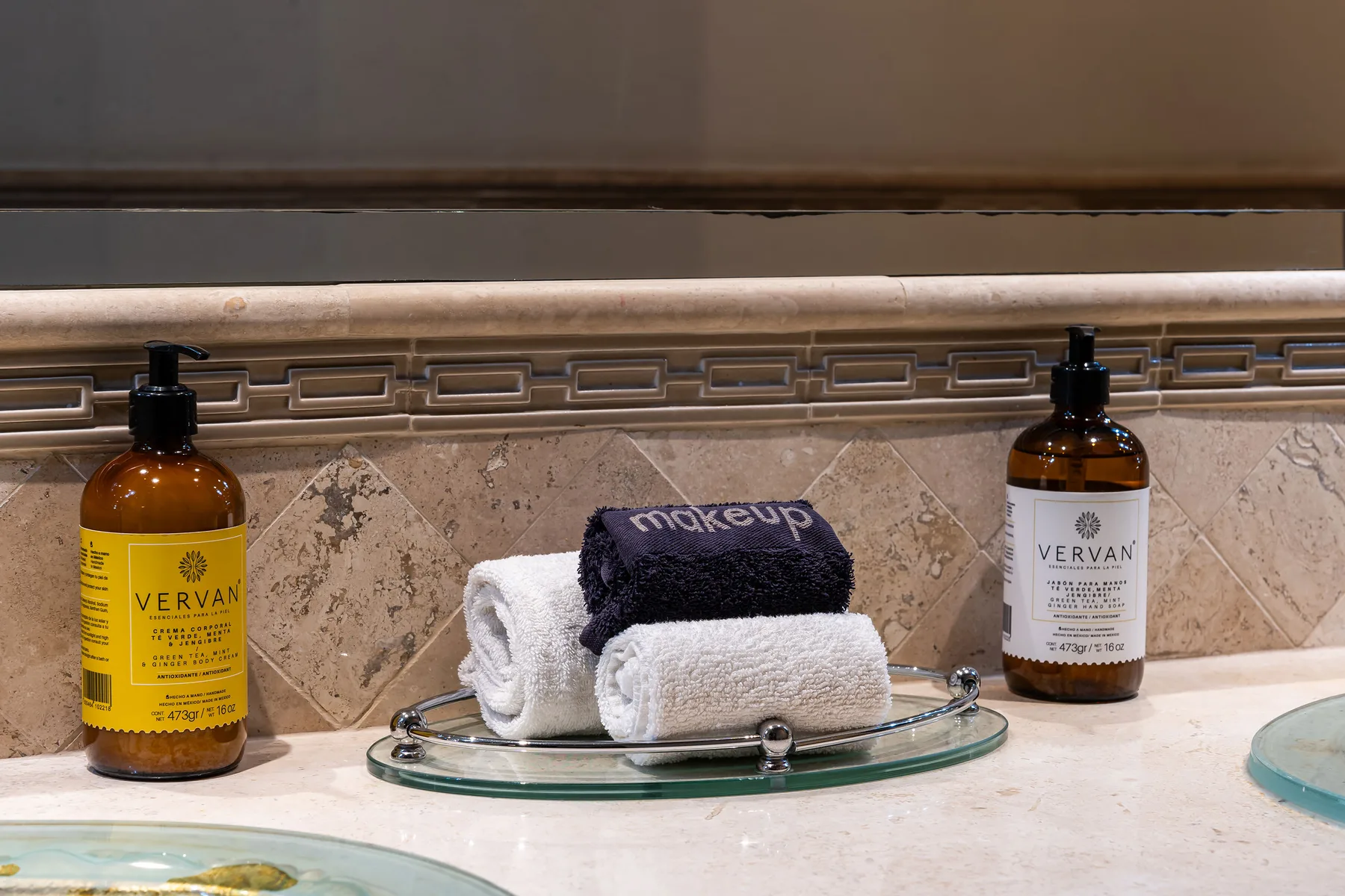 A bathroom vanity with soap dispensers and folded towels on a glass tray.