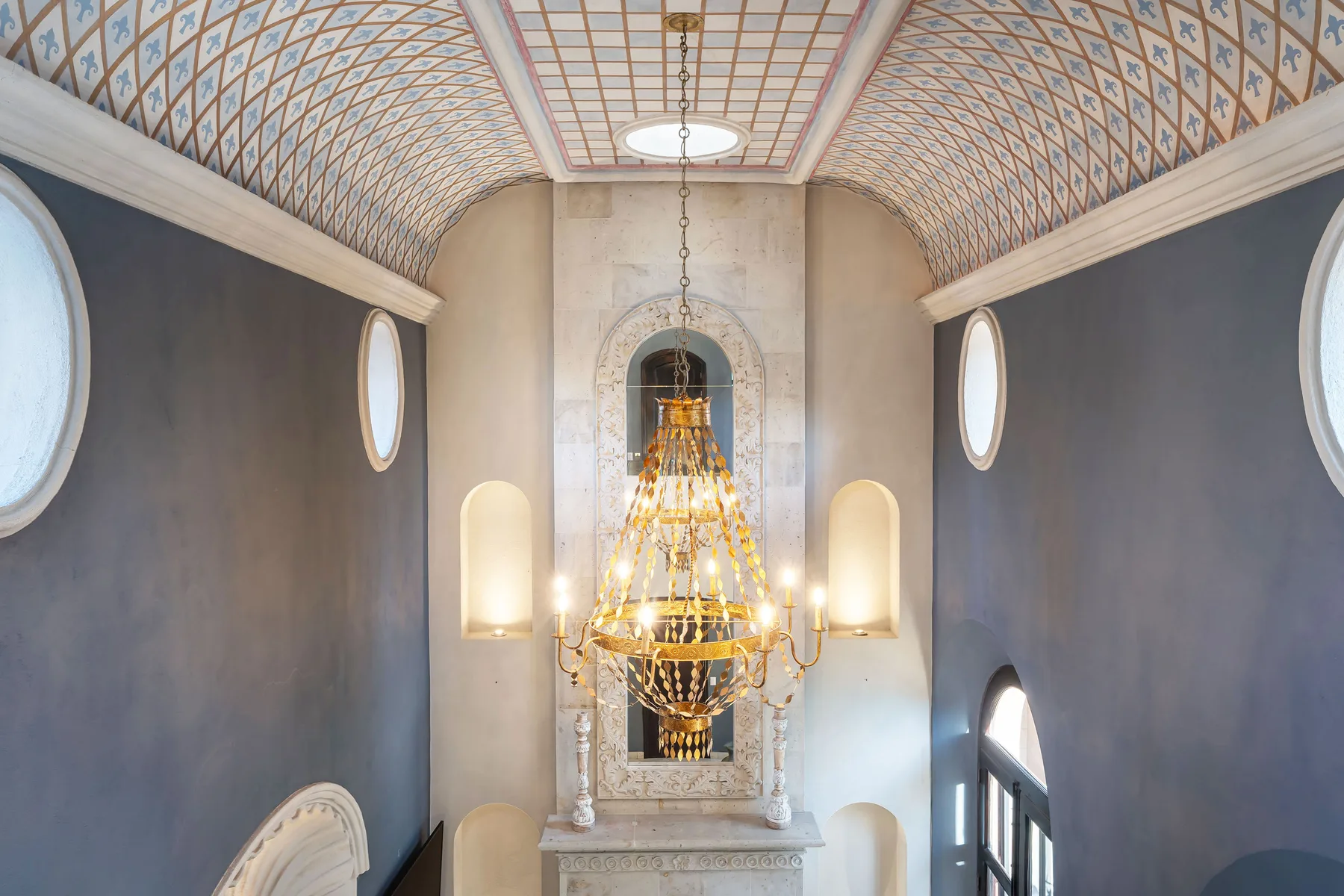 A decorative interior hall with a large chandelier hanging above a fireplace.