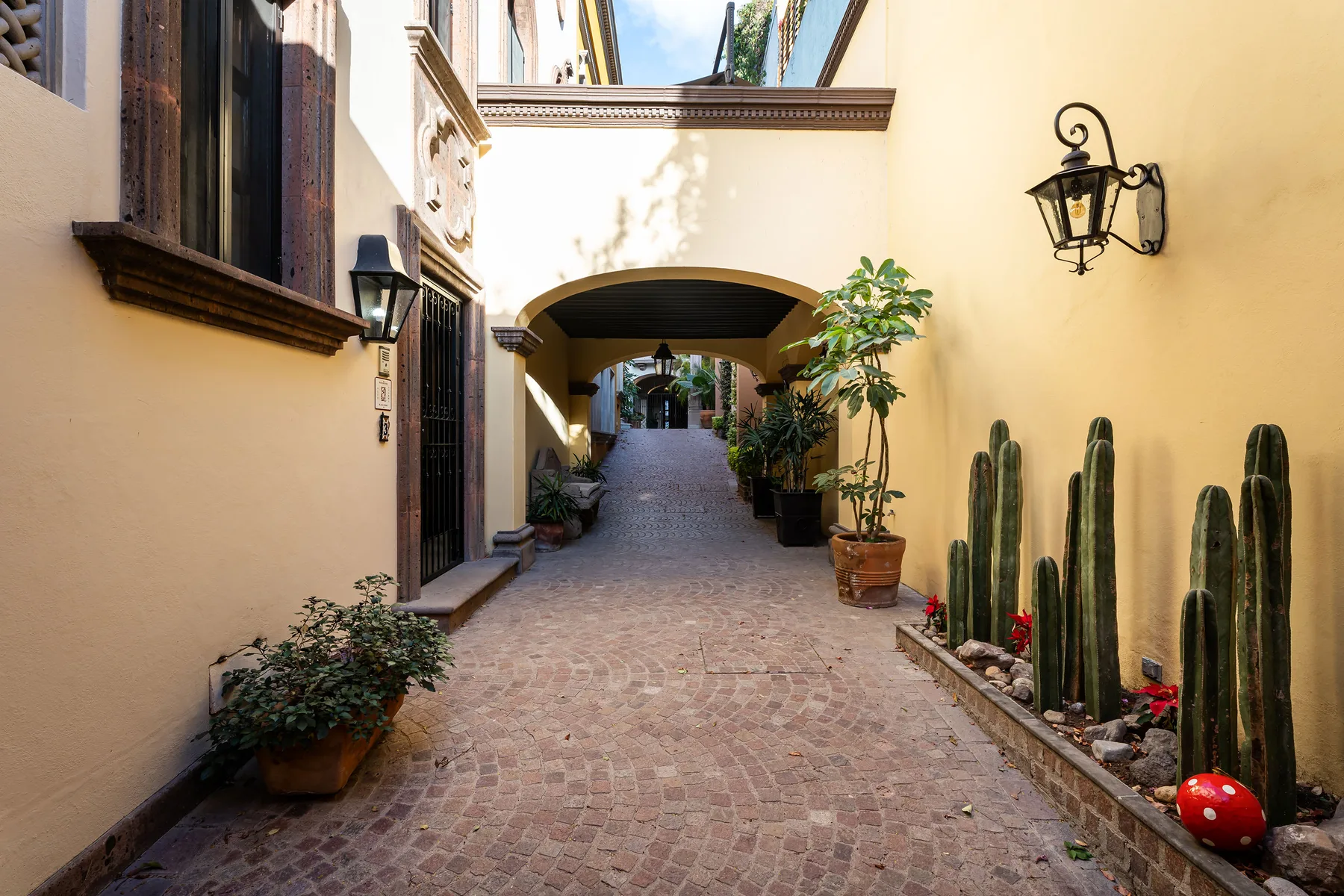Shared amenity: A paved courtyard passage runs beneath an arch, with potted plants along the walls.